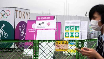 A man walking with a mask on in Tokyo with health warning signs regarding COVID on the back