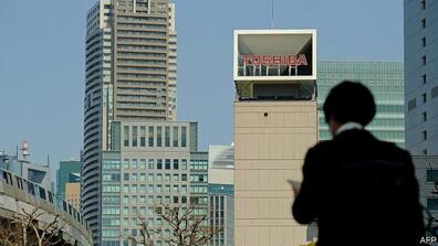 A person looking at a building in the view, and on top of the building it says "Toshiba"