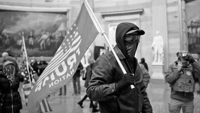 A masked man holding a flag that writes "Trump Nation" on it