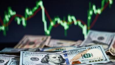 A pile of money in front of stock market trendlines 