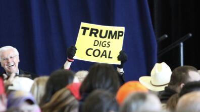 Person holding a sign that reads "Trump digs coal"