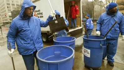The Doe Fund workers pick up their garbage pails on a Manhattan street corner before heading out to clean the streets, on Feb. 10, 2005, in New York