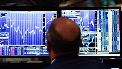 A man looking at two computer screens that show stock screens