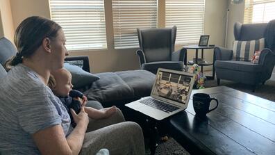 a parent holds a baby while on a Zoom call
