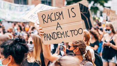 a protester holds up a sign that reads "racism is a pandemic"
