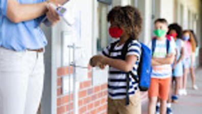 Kids entering school following COVID guidelines, with their masks on, sanitizing their hands and getting their temperatures checked