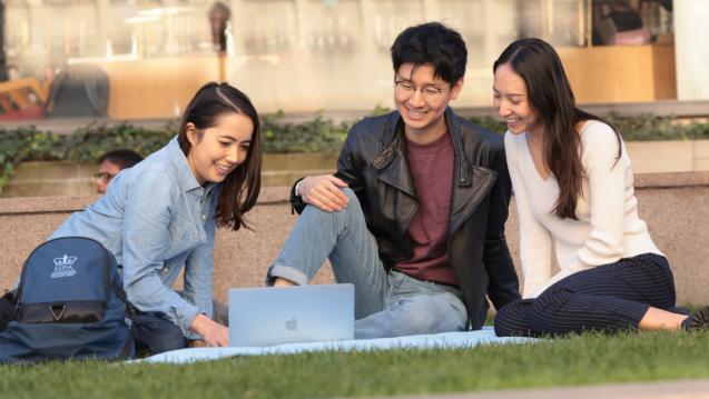 Students sitting on ground talking and looking at a laptop together